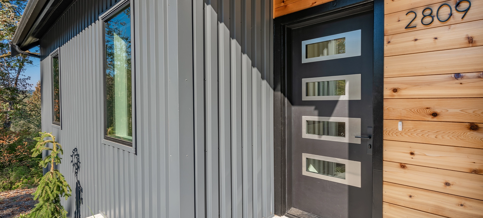 front door entry exterior of a contemporary home with grey metal siding black entrance and cedar siding