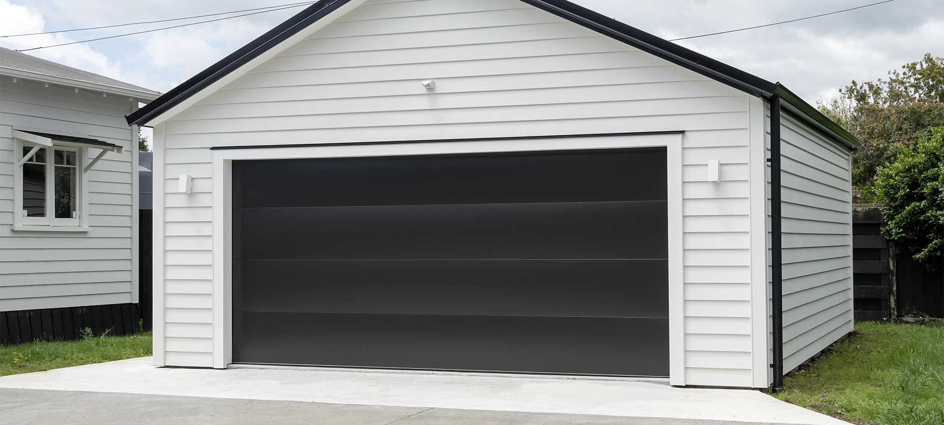 double white garage with gable roof and black tilt-up retractable raised panel metal door