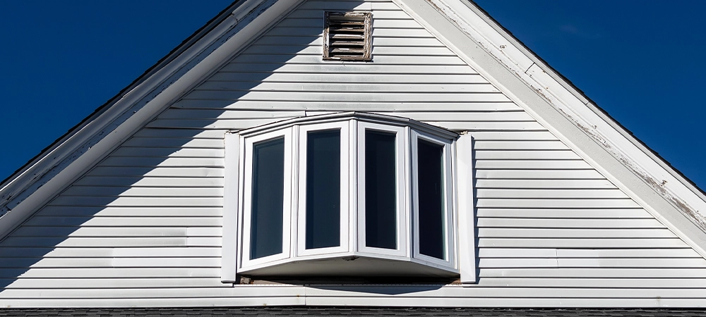 Old house attic bow window and small air vent against clear blue sky