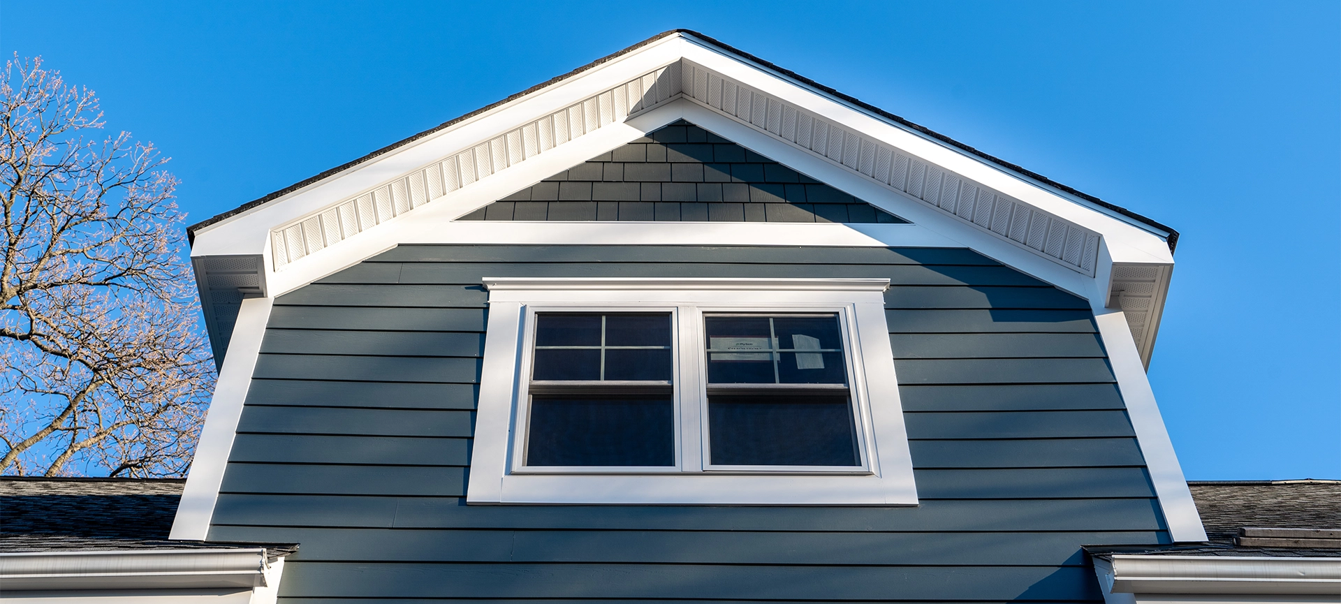 New restoration facade with double hung window w/ fixed top sash and bottom sash that slides up, divided by two white grilles, thick elegant frame, blue vinyl siding contrasting white corner, gable