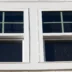 Double hung window with fixed top sash and bottom sash that slides up, sash divided by white grilles a surrounded by white elegant frame horizontal white shingle siding on new construction residence